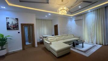 A modern living room with a sectional sofa, a dining table, and a chandelier.