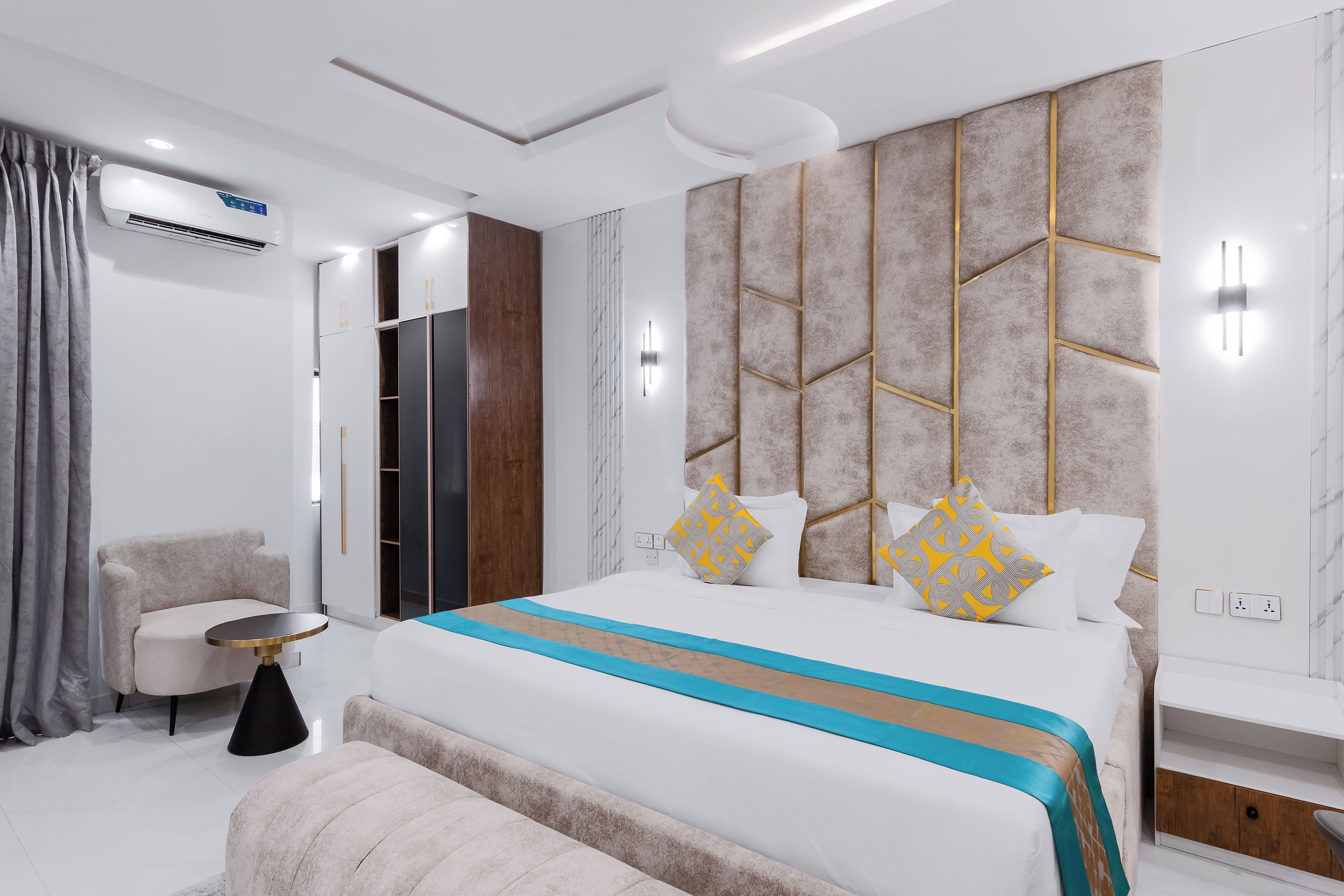 A modern bedroom with a large bed, bedside tables, a wardrobe, and an air conditioning unit.