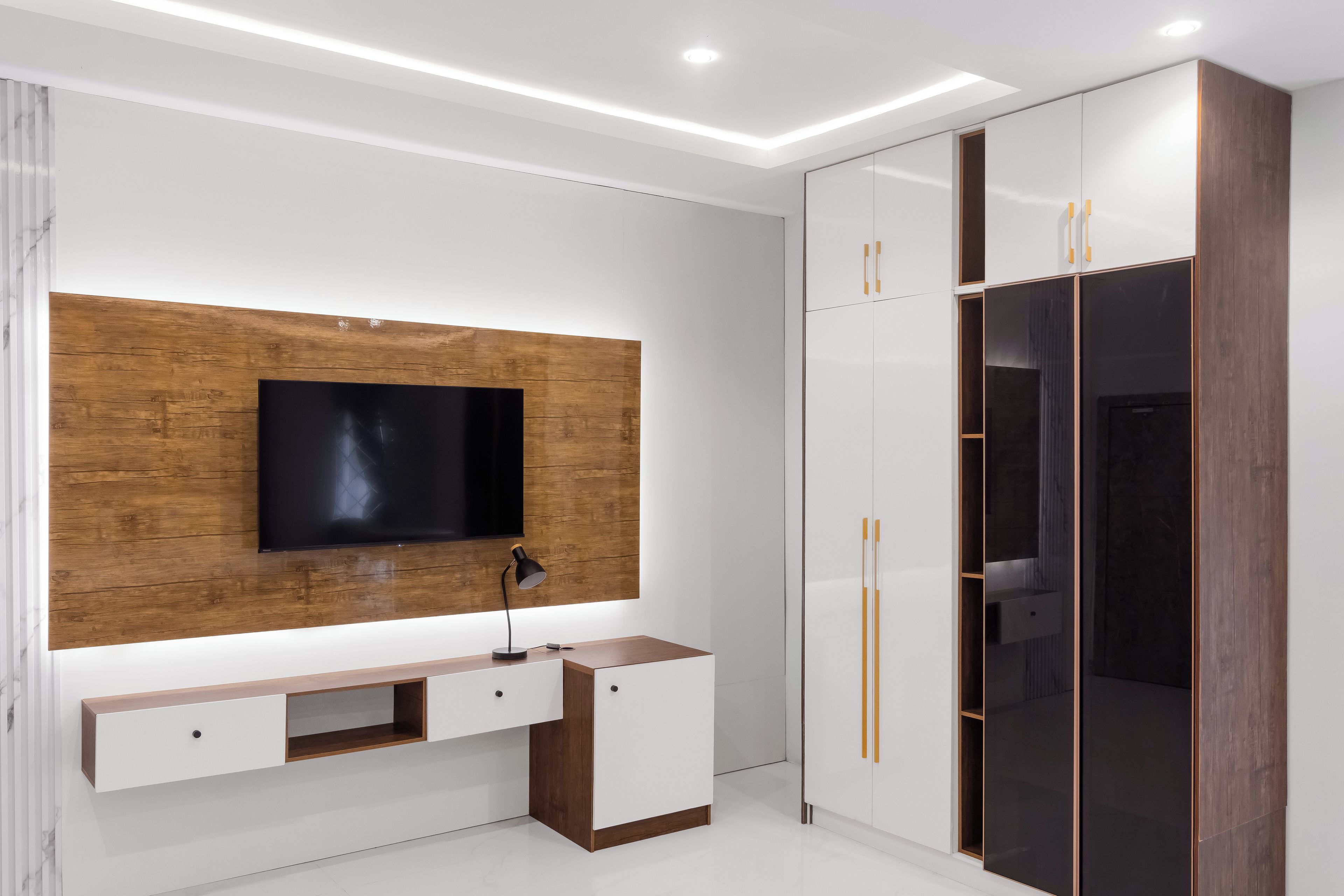A modern bedroom with a built-in TV, a wooden accent wall, a bedside table, and a wardrobe with mirrored doors.