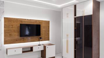 A modern bedroom with a built-in TV, a wooden accent wall, a bedside table, and a wardrobe with mirrored doors.