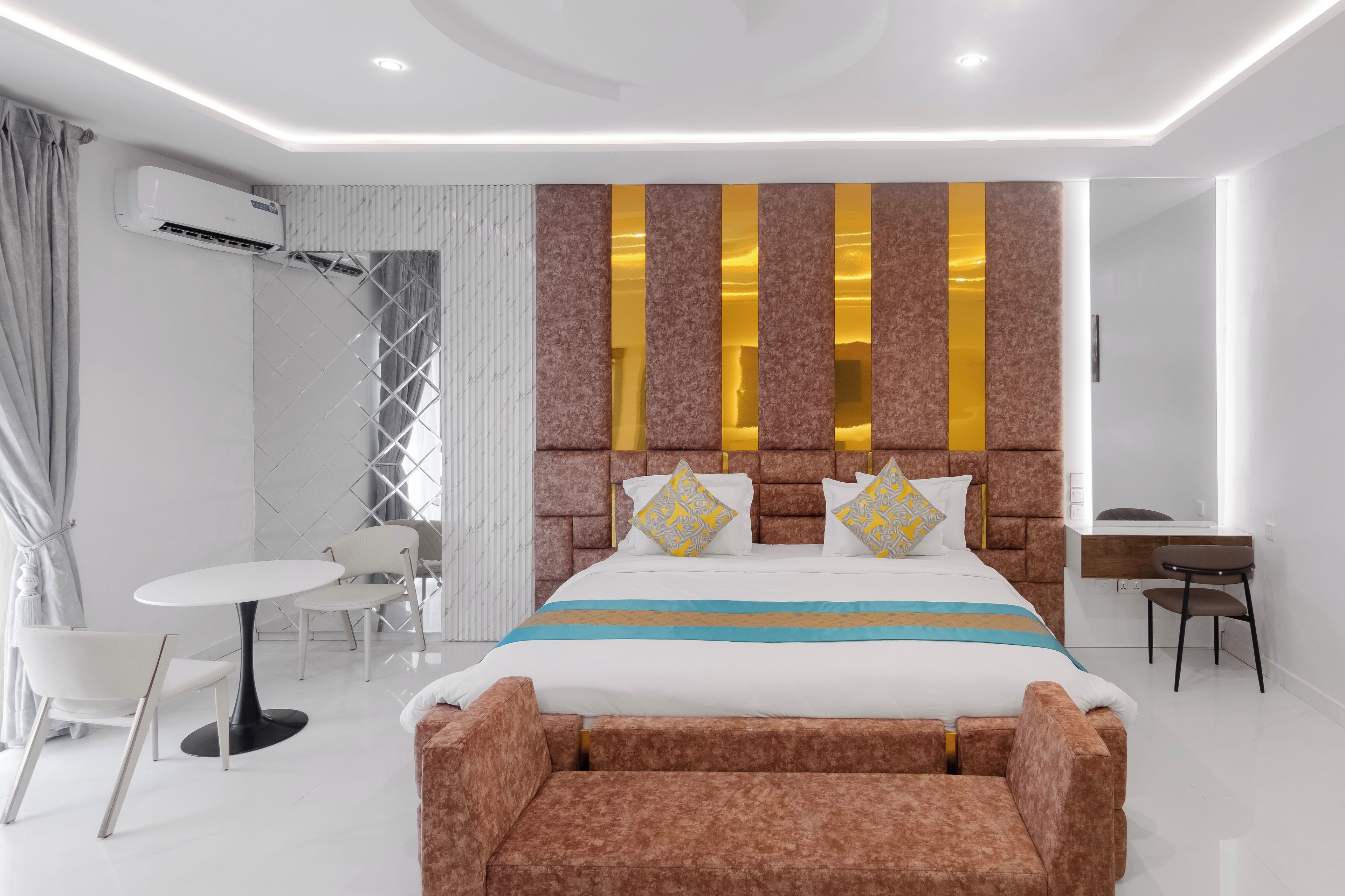 A modern hotel room with a large bed, a desk, a chair, and a small table.