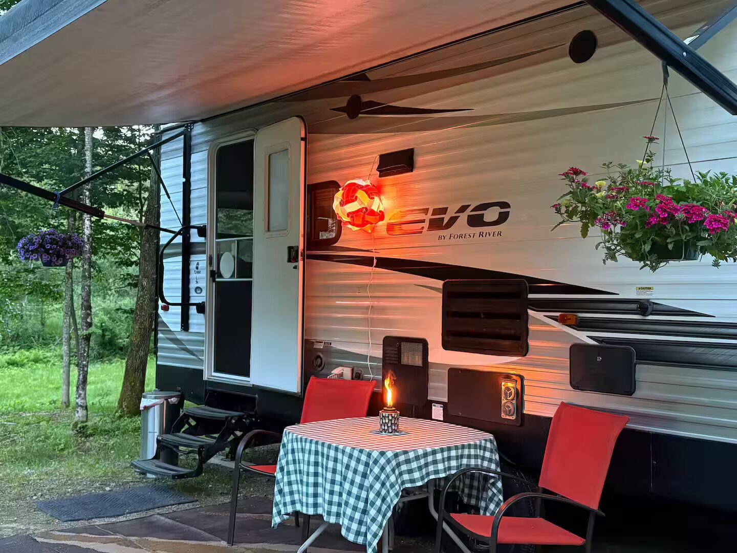A covered RV with a table and chairs, a hanging flower basket, and a 'EVO' logo.