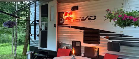 A covered RV with a table and chairs, a hanging flower basket, and a 'EVO' logo.