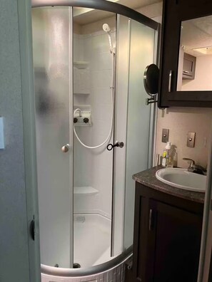A bathroom with a glass-enclosed shower, a sink, and a mirror. - RV camp site great area to hunt, fish, boat, relax


with AC (Mercer)