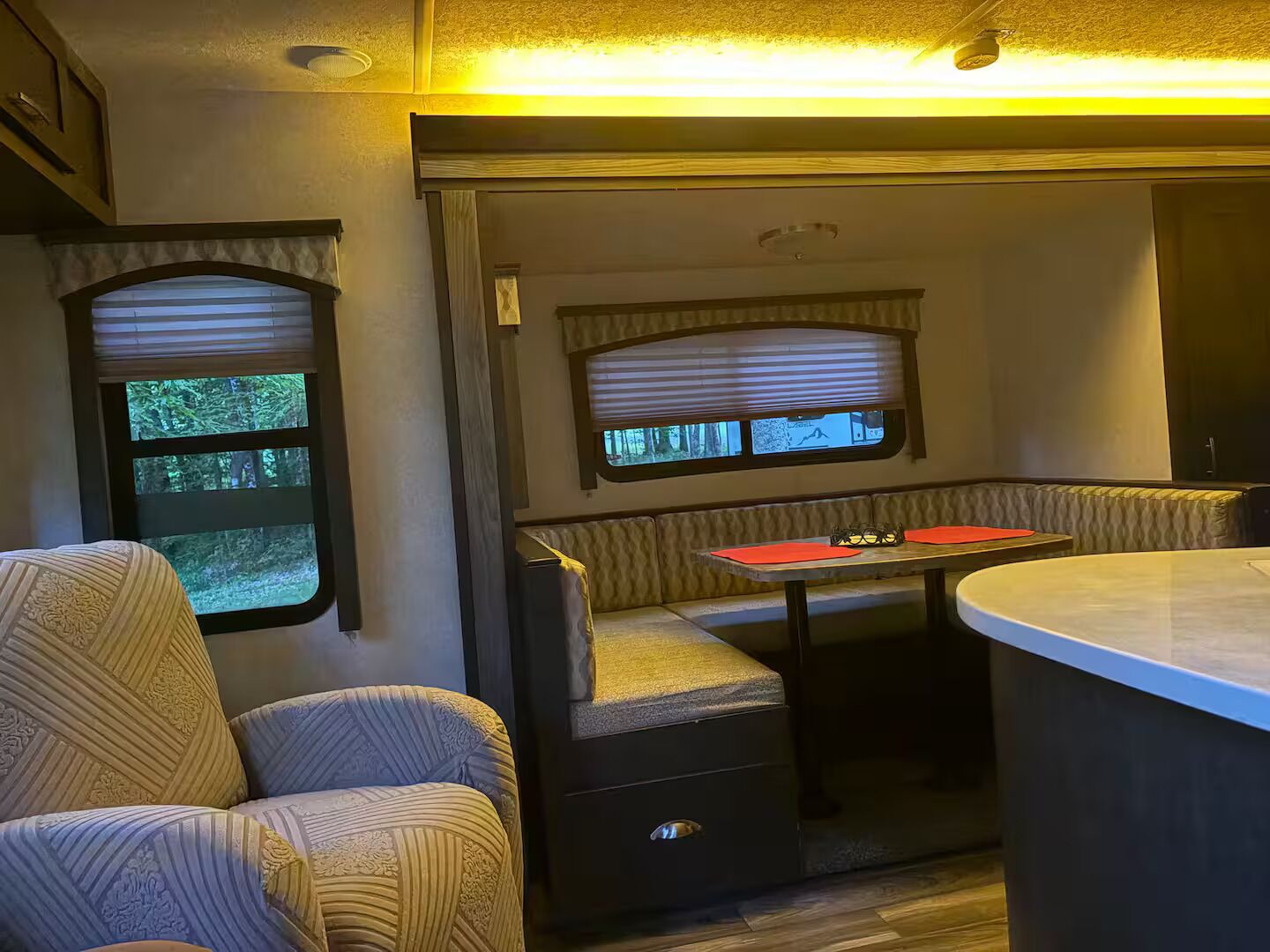 A cozy RV interior with a seating area, a table, and windows with blinds.