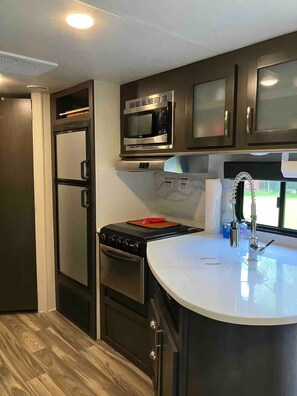 A compact kitchen with a refrigerator, stove, microwave, and a sink with a faucet. - RV camp site great area to hunt, fish, boat, relax


with AC (Mercer)