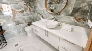 Un baño con tocador blanco, espejo redondo y paredes con diseño de mármol.