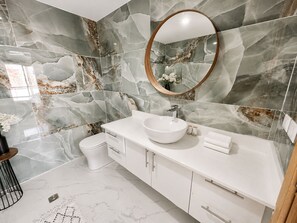 A bathroom with a white vanity, a round mirror, and marble-patterned walls. - Private Pool Villa 3BR | Gated, 10 Min Downtown (Punta Cana)