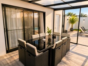 A glass-enclosed patio with a dining table and chairs, a potted plant, and a view of the pool and palm trees. - Private Pool Villa 3BR | Gated, 10 Min Downtown (Punta Cana)
