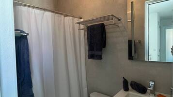 Un bagno con tenda doccia, un portasciugamani con asciugamano, un water e un lavandino con specchio.