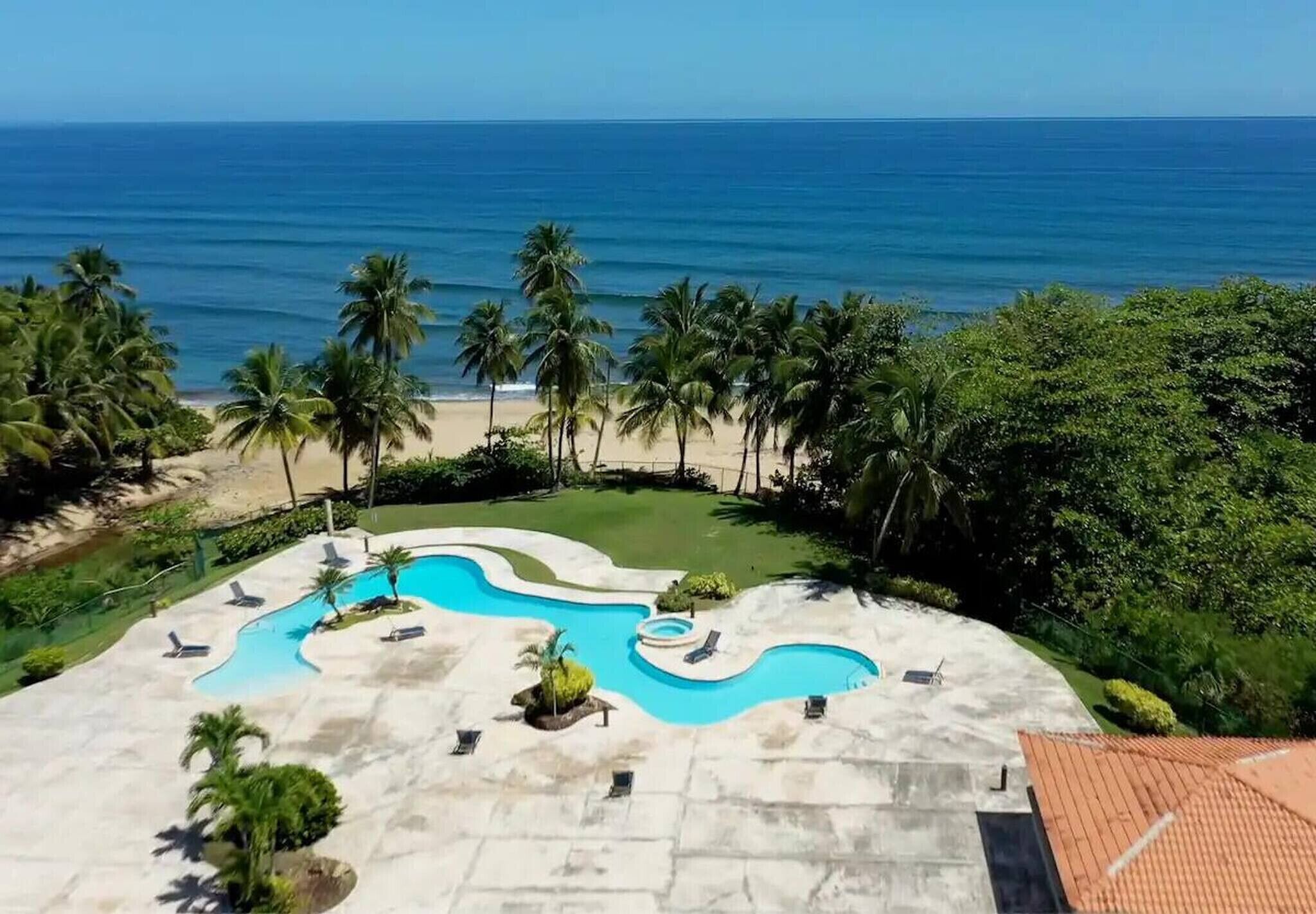 A resort with a swimming pool, palm trees, and a view of the ocean.
