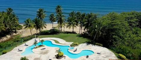 A resort with a swimming pool, palm trees, and a view of the ocean.