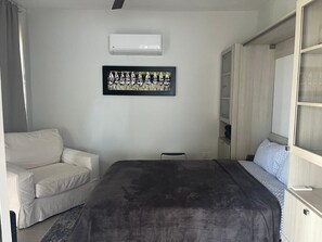 A bedroom with a bed, a white sofa, a small table, and a wardrobe.