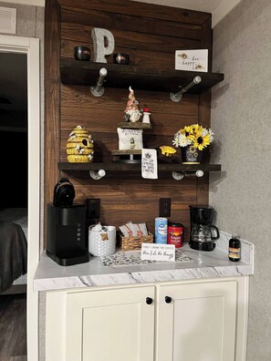 Un comptoir de cuisine avec une machine à café, un panier de collations et un panneau sur lequel on peut lire : « D’abord, je bois mon café, puis je m’occupe du reste. »
