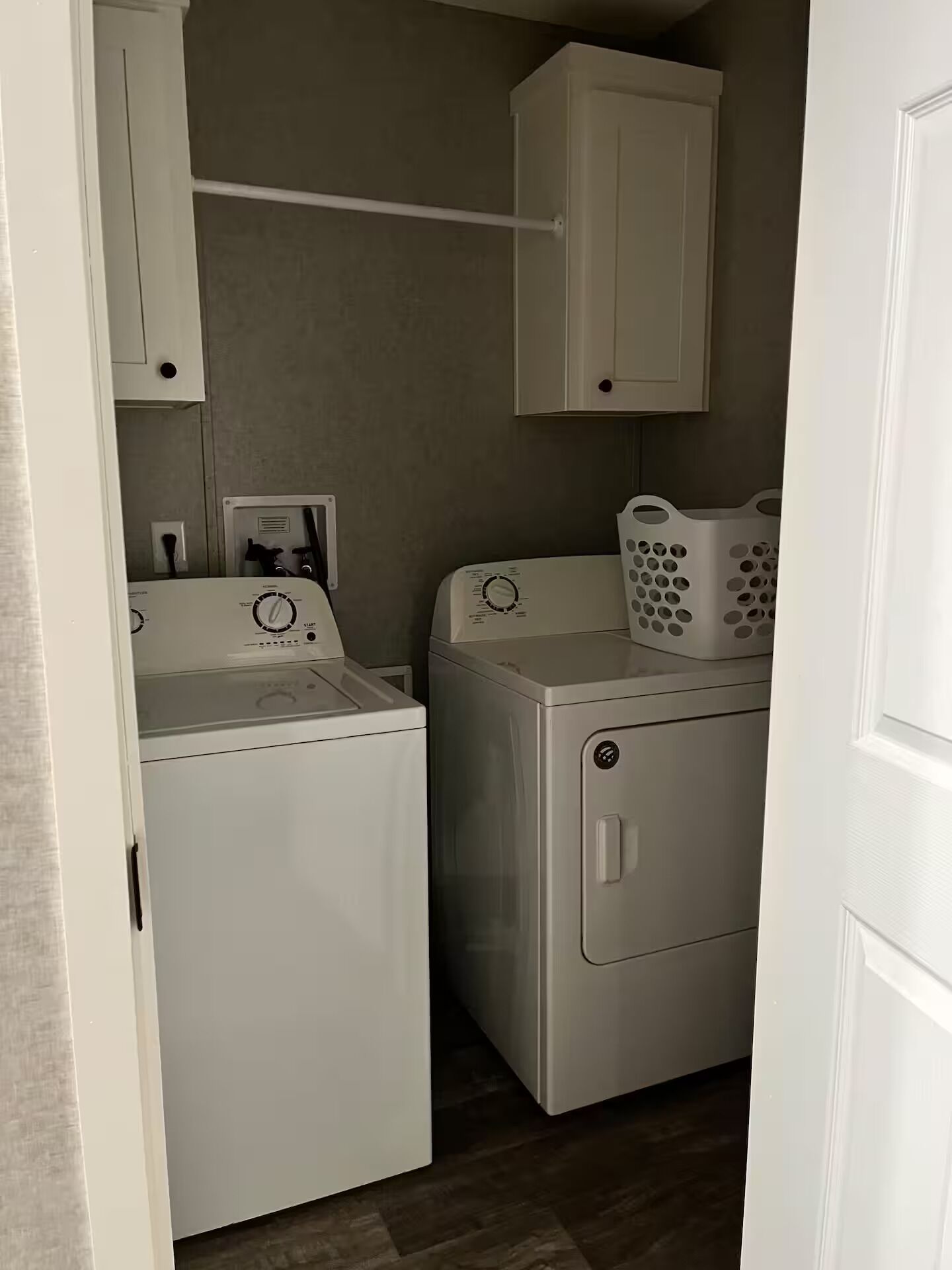 Une buanderie avec deux machines à laver blanches, un meuble blanc au-dessus des machines et un panier à linge sur la droite.