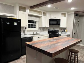 A kitchen with white cabinets, a black refrigerator, a black microwave, a stove, and a wooden island with stools. - Quiet country setting, river retreat dunnellon (Dunnellon)