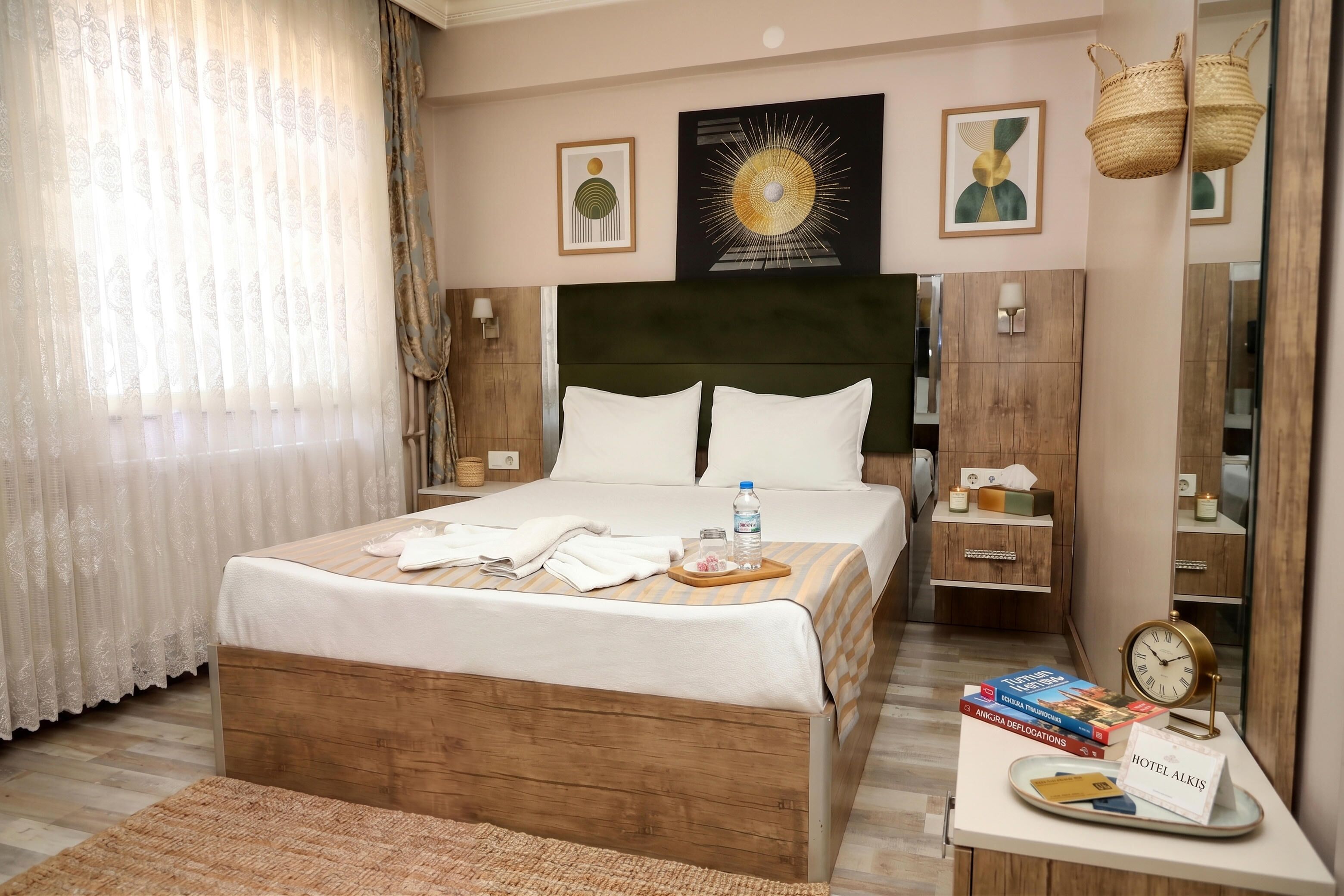 Ein Hotelzimmer mit Bett, Nachttischen, einem Spiegel, Kunstwerken an der Wand und einem Schild mit dem Hotelnamen.