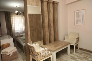 Habitació amb un llit, un separador de fusta, taula, dues cadires, un quadre al mur i una làmpada al sostre.