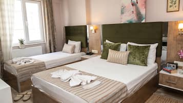 Quarto de hotel com duas camas, janela com cortinas, radiador, uma pequena planta e um quadro na parede.