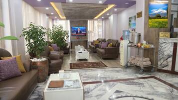 A hotel lobby with a reception desk, seating area, and a television screen.