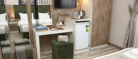 A hotel room with a bed, a desk with a computer, a television, a minibar, and a small seating area.
