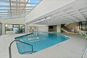 An indoor swimming pool with a clear ceiling, a seating area with tables, and a staircase leading to an upper level. - Luxury 2/2 Oceanfront at Sea Winds PH8 (North Myrtle Beach)