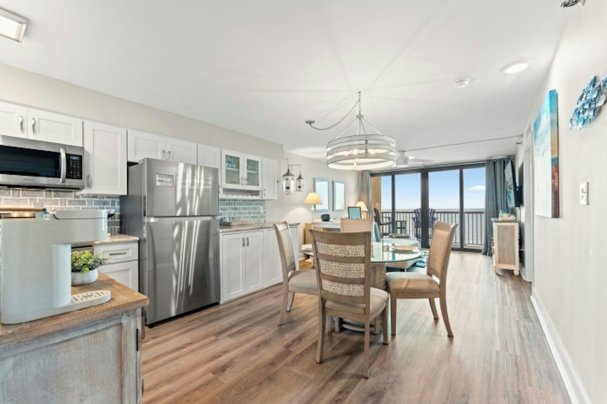 A modern kitchen with stainless steel appliances, a dining area with a glass table, and a balcony with a view.