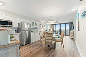 A modern kitchen with stainless steel appliances, a dining area with a glass table, and a balcony with a view. - Luxury 2/2 Oceanfront at Sea Winds PH8 (North Myrtle Beach)