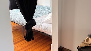 Une chambre à coucher avec un lit, un plancher en bois, un mur blanc et un rideau noir.