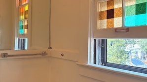 Une salle de bain avec un meuble-lavabo en bois, un lavabo blanc, un miroir et une fenêtre ornée de vitraux colorés.