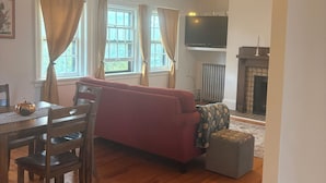 Un salon avec un canapé rouge, une table à manger en bois entourée de chaises, une cheminée et un téléviseur fixé au mur.