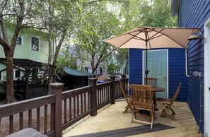 Eine Holzterrasse mit Tisch und Stühlen, einem Sonnenschirm und einer blauen Tür.