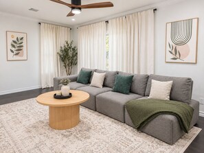 A modern living room with a grey sofa, a round wooden coffee table, and a green throw blanket. - Oak & Ash | Lindale Park Houston (Houston)