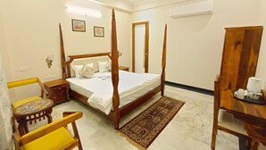 A bedroom with a four-poster bed, a wooden chair, a bedside table, and a small table with a tray. - Gupta Vilas - A Boutique Homestay -  Standard King Room 3 (Agra)