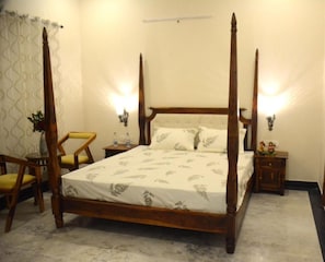 Una cama con dosel, un edredón blanco, dos mesitas de noche con lámparas, una silla y una pequeña mesa con una planta.