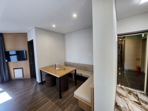 A modern hotel room with a wooden table, a bench, a flat-screen TV mounted on the wall, and a marble-patterned floor. - seombadi hotel (Ulleung)