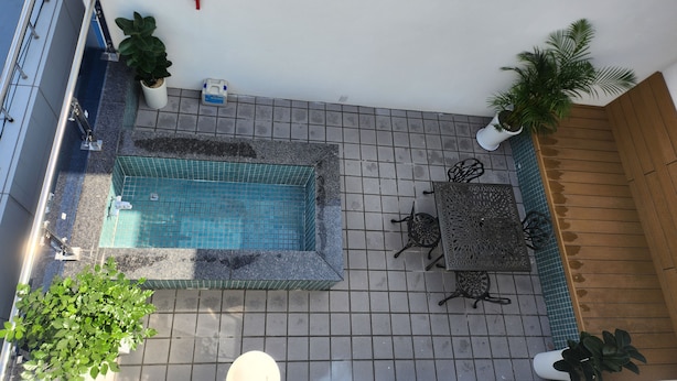 Un área de piscina en la azotea con piso de baldosas, piscina, plantas en macetas y mobiliario exterior.