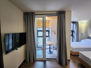Et hotelværelse med et fladskærms-tv, en seng, et lille bord med en stol og en skydedør, der fører til et udendørs område.