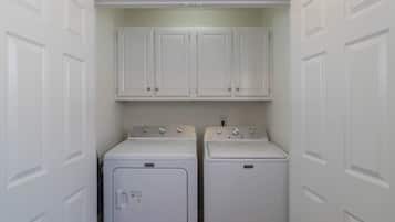 A laundry room with two stacked washers and dryers, white cabinets above, and white doors on either side.