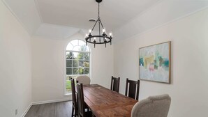 A dining room with a wooden table and chairs, a chandelier, a large window, and a painting on the wall. - Tanner Drive Getaway | Pet Friendly (Oxford)