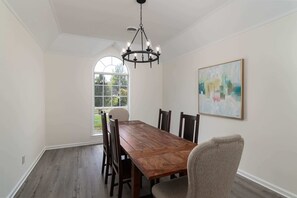 A dining room with a wooden table and chairs, a chandelier, a large window, and a painting on the wall. - Tanner Drive Getaway | Pet Friendly (Oxford)