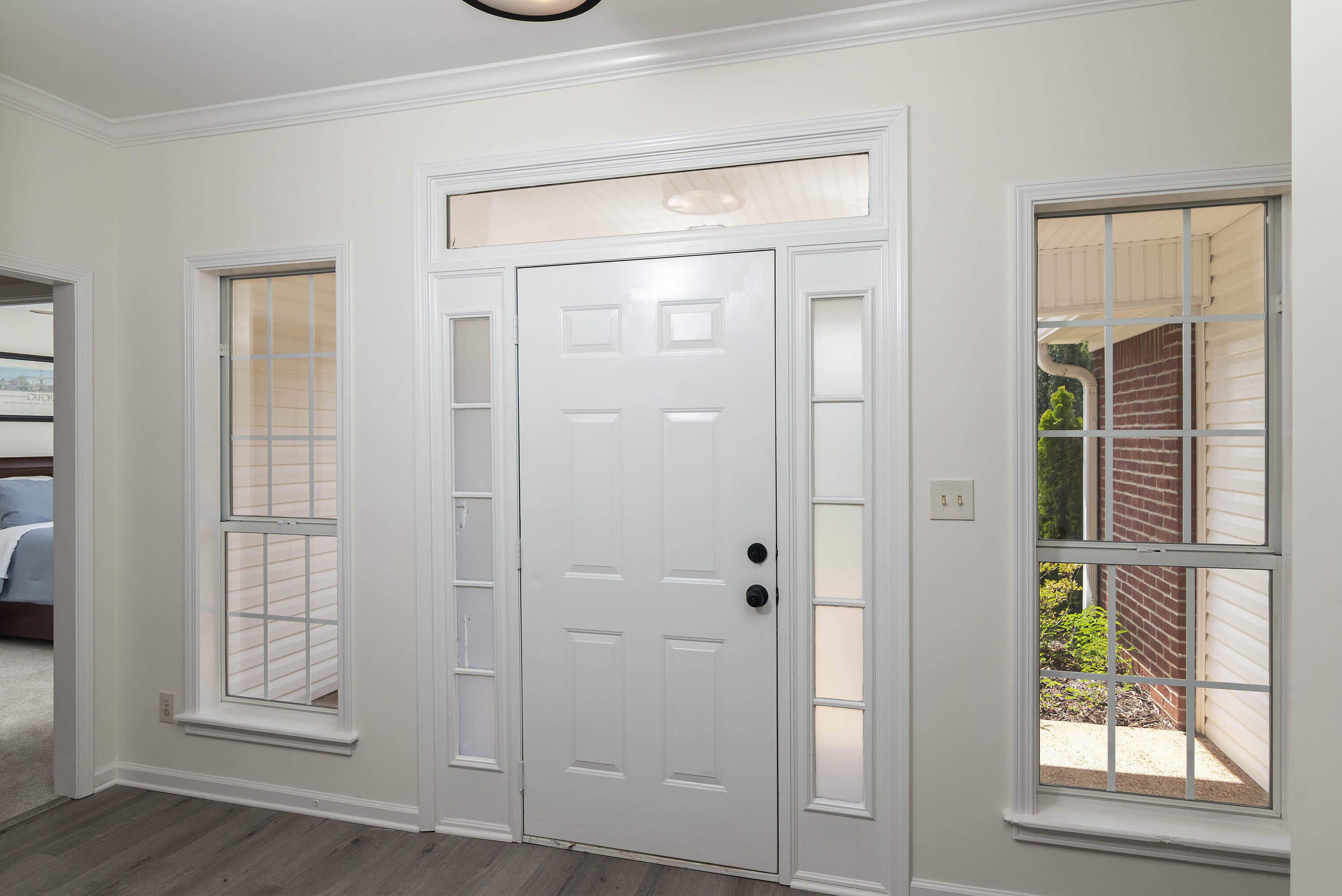 A white door with a glass panel and a window with a grid pattern on the wall.