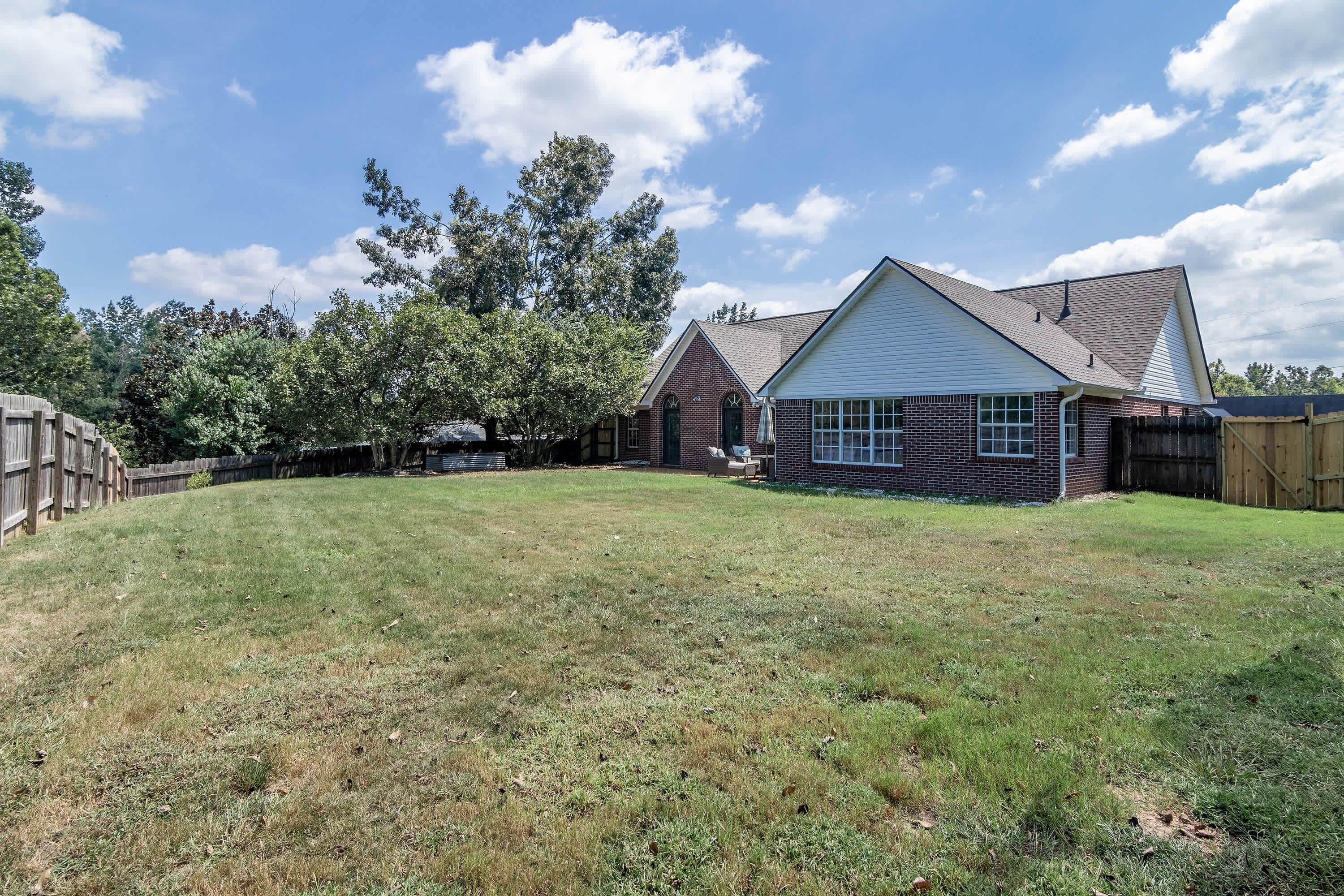 A residential property with a grassy backyard, a brick house, and a wooden fence.
