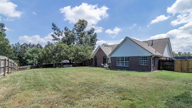 A residential property with a grassy backyard, a brick house, and a wooden fence. - Tanner Drive Getaway | Pet Friendly (Oxford)
