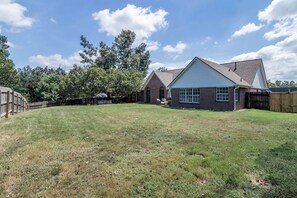 A residential property with a grassy backyard, a brick house, and a wooden fence. - Tanner Drive Getaway | Pet Friendly (Oxford)