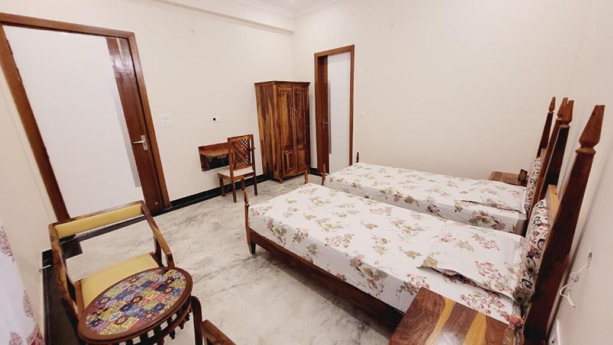 A bedroom with two beds, a wooden wardrobe, a chair, and a small table.