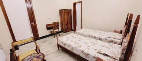 A bedroom with two beds, a wooden wardrobe, a chair, and a small table.