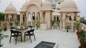 Eine Terrasse mit Tisch und Stühlen, umgeben von Blumentöpfen und einem Gebäude mit Kuppelbau.