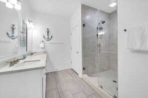 A modern bathroom with a glass-enclosed shower, a double vanity with a sink and mirror, and decorative wall art. - 🦀Seabreeze | Walk to Beach | Community Pool | 3BR🌅 (Panama City Beach)