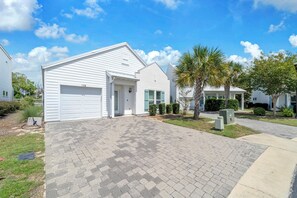 A residential house with a garage, a front yard with a paved driveway, and a small garden area with palm trees. - 🦀Seabreeze | Walk to Beach | Community Pool | 3BR🌅 (Panama City Beach)